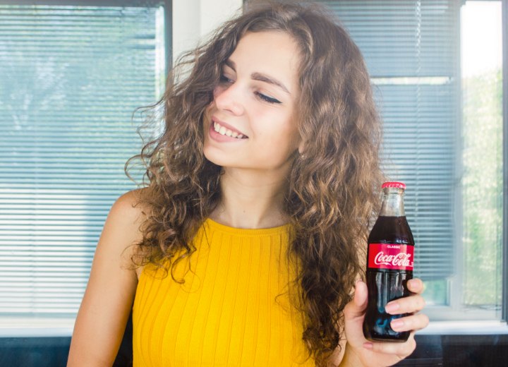 Vrouw met lang krullend haar die Cola drinkt