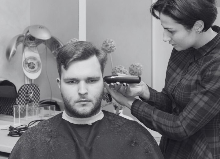 Man onder een kapperscape terwijl de kapster knipt